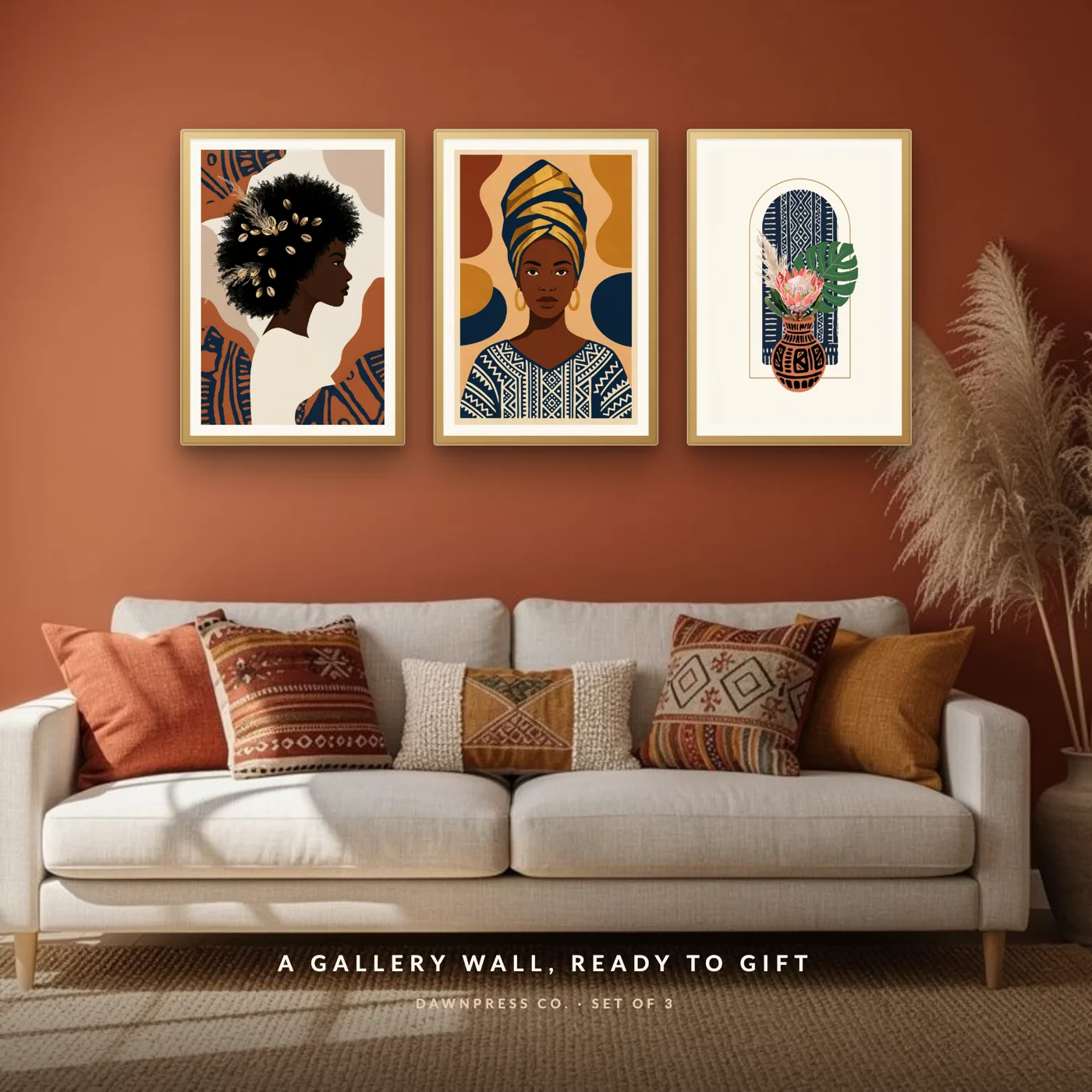 Three gold-framed Afrohemian art prints of Black women and mudcloth patterns above a cream sofa on a terracotta wall